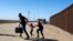 Una familia de migrantes de Cuba cruza corriendo la frontera por el muro que separa a Estados Unidos y México para entregarse a las autoridades el 13 de mayo de 2021 en Yuma, Arizona. (Foto de RINGO CHIU / AFP)
